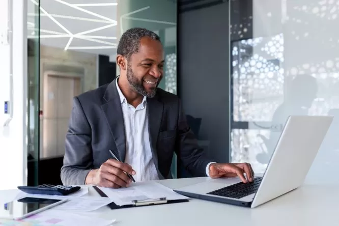 Successful satisfied financier behind paper work, senior experienced filling out documents, using calculator for calculation, businessman behind paper work inside office smiling.